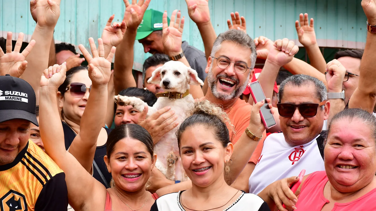 Clécio no meio da população, todos sorrindo com as mãos levantadas